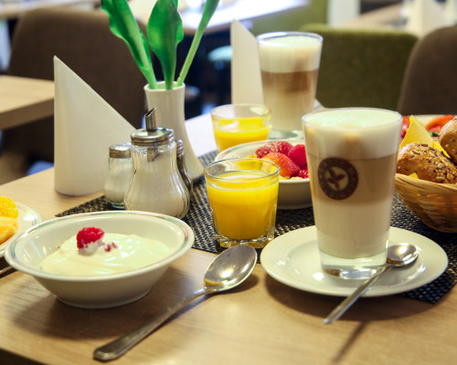 Ein gemütliches Frühstück mit Joghurt, Früchten, Kaffee, Orangensaft und Gebäck auf einem Tisch.